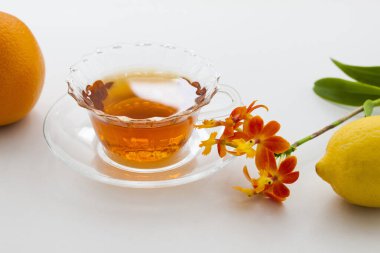 Cam fincanda çay ve beyaz arka planda çiçekler..