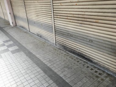 Kapalı metal panjurlar ve kaldırımları gösteren boş sokak görüntüsü