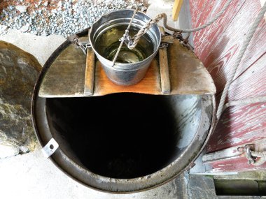 Karanlık kuyunun üzerinde asılı duran metal kova.