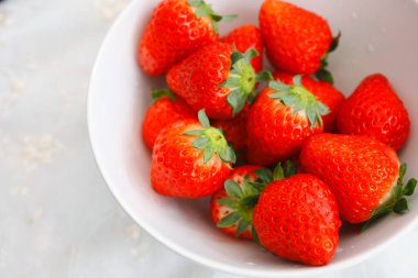 Masadaki beyaz kasede taze kırmızı çileklerin yakın plan görüntüsü.     