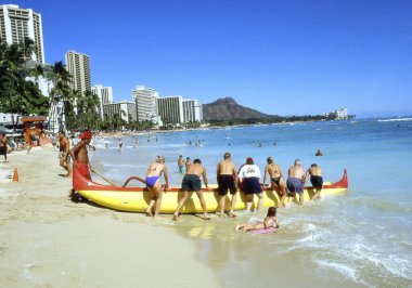 İnsanlar kumsalda dinleniyor, oteller ve palmiyelerle.