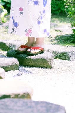 Kimono giyen ve bahçede sandalet giyen genç bir kadın.