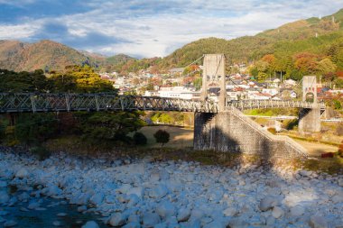 Küçük kasaba tepelerinin yakınındaki kayalık nehri geçerken asma köprü.