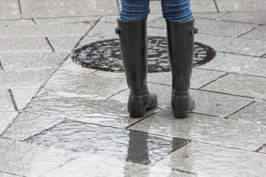 Islak kaldırımda çizme giyen bir kadın.