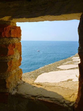 Antik tuğla duvarın dar bir penceresinden deniz manzarası