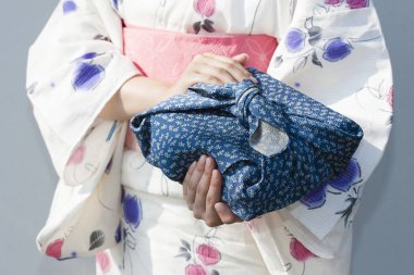 Mavi Furoshiki 'ye sarılı bento tutan kimono giyen genç bir kadın.
