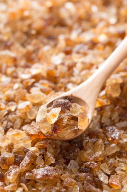 Yakından bakınca kahverengi şeker kristalleri ve tahta kaşık görünüyor.