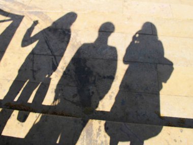 Açık havada birlikte duran üç kişinin gölgeleri.