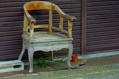 Açık havada kahverengi metal panjurların yanında duran yıpranmış ahşap sandalye.