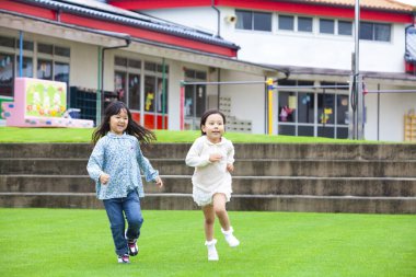 İki gülümseyen Asyalı küçük kızın portresi yeşil çimlerde koşuyor.