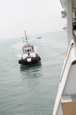 Küçük römorkör, sakin su yüzeyinde büyük bir gemiyi çekiyor.