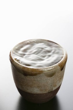 Beyaz zemin üzerinde temiz su bulunan kahverengi seramik bardak