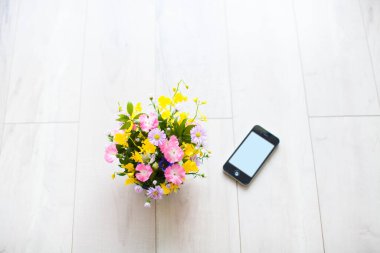 Vazoda güzel çiçekler ve ahşap zeminde akıllı telefon.