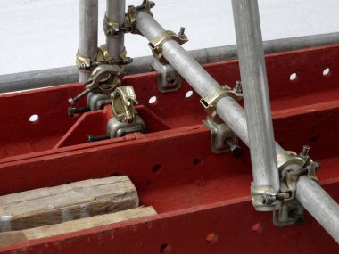 Dışarıdaki kırmızı çelik kirişlere bağlı metal iskele boruları.