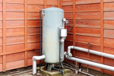 Dışarıda tahta duvarın yanında duran büyük metal basınç tankı.