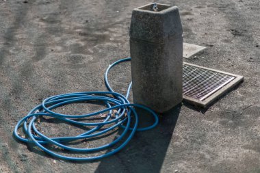 Beton su çeşmesi ve güneş panelinin yanında duran mavi hortum.