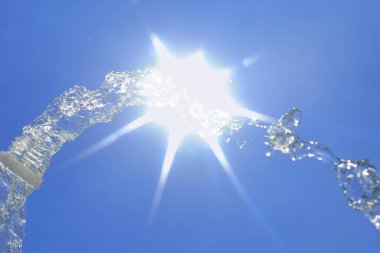 Mavi arka planda güneşe karşı şişeden temiz su sıçraması