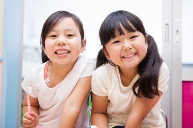 İki küçük Asyalı kız dişlerini birlikte fırçalıyorlar.