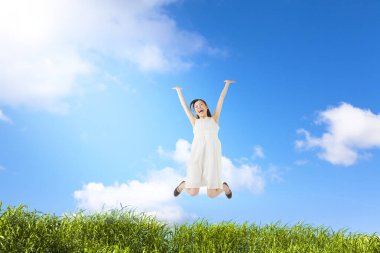 Mutlu genç kadın yeşil çayırda havada zıplıyor.