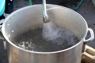 Açık hava hortumuyla su dolduran büyük metal tencere.