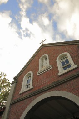 Tuğla kilise cephesinde kemerli pencereler gökyüzüne karşı çapraz heykel