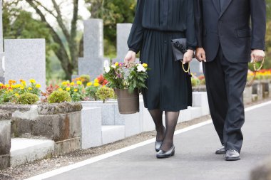 Bir kadın ve bir erkek mezarlıktaki mezara bir kova çiçek taşıyorlar..