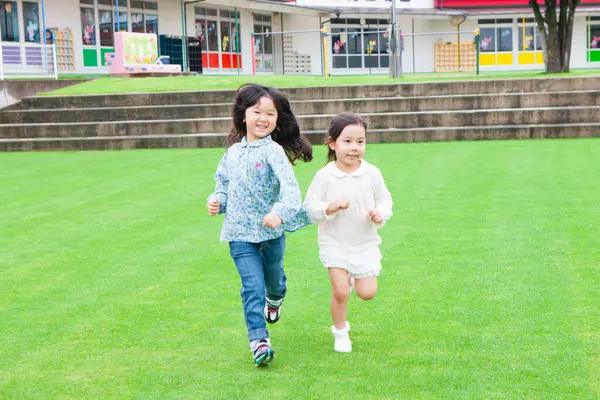 緑の草の上を走っている2人の笑顔のアジアの少女の肖像画 — ストック写真