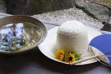 Ayçiçekleri ve mavi yelpazenin yanında duran hasır şapka