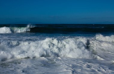 Büyük deniz dalgaları kayalık plajı eziyor.