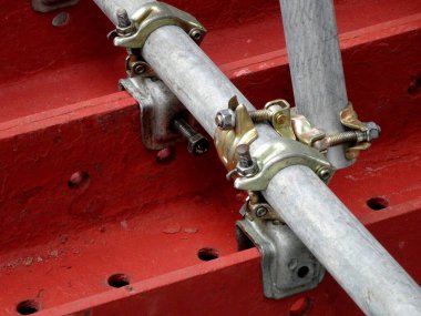 Metal kıskaçlar kırmızı endüstriyel yüzeydeki boruları emniyete alıyor