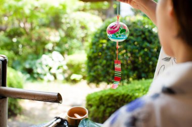 Geleneksel Japon kimonosu giyen genç bir kadın yaz bahçesinde asma süslemesi tutuyor. 