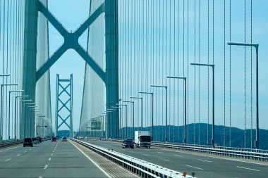 Araçlar mavi gökyüzünün altında büyük asma köprüden geçiyor.