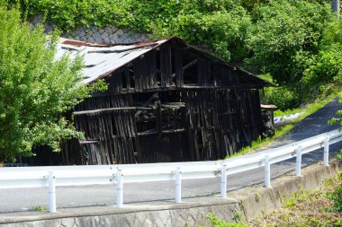 Eski ahşap ahır yeşil ağaçların arasında dolambaçlı kırsal yolun yanında duruyor.