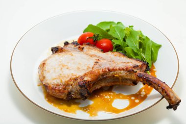 Domatesli domuz kaburgası ve beyaz tabakta roka. 