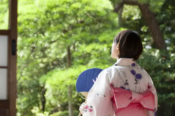 Japanese woman wearing kimono sitting on engawa and looking at garden