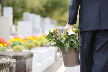 Bir adam mezarlıktaki mezara kadar kovayla çiçek taşır..