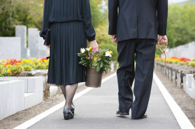 Mezarlıktaki cenaze sırasında ellerinde çiçek taşıyan siyah kostümlü bir çift. 