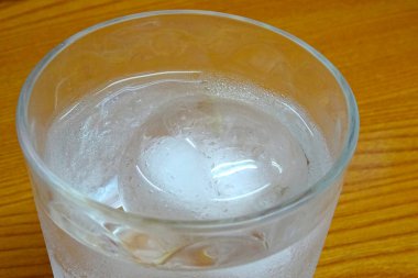 Ahşap masanın üzerinde buz küpleri olan bir bardak suyun yakın görüntüsü.    