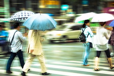 Şehir caddesinde yağmurda yürüyen şemsiyeli insanların bulanık görüntüsü                   