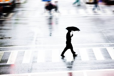 Yağmurlu bir günde şehir caddesinde yürüyen siluetli insanlar        