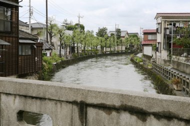 Bulutlu gökyüzünün altında sakin bir nehir Japon mahallesinden akıyor.