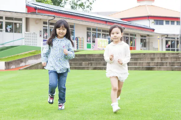 緑の草の上を走っている2人の笑顔のアジアの少女の肖像画 — ストック写真