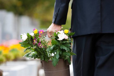 Bir adam mezarlıktaki mezara kadar kovayla çiçek taşır..