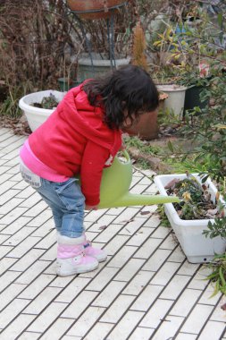 Arka bahçede çiçek sulayan küçük bir kız.