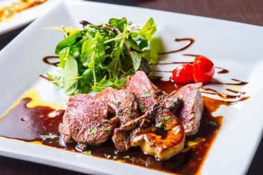 Soslu ızgara et ve beyaz tabakta yeşillikler.