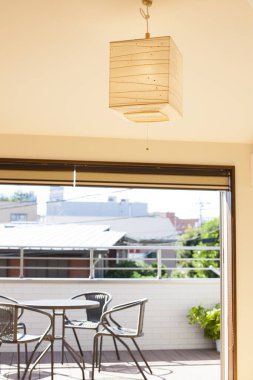 Boş yuvarlak masa, terasta sandalyeler ve odada zarif tavan lambası.