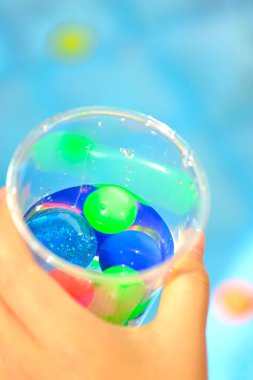 Çocukların elleri renkli küçük toplarla plastik bardakları tutuyor.