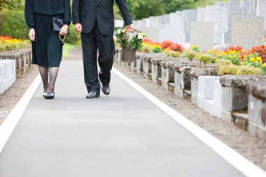 Siyah giysili kadın ve erkek mezarlıkta çiçek sepeti taşıyorlar.