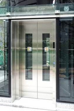 Modern cam asansör kapıları şehir çevresini yansıtıyor.