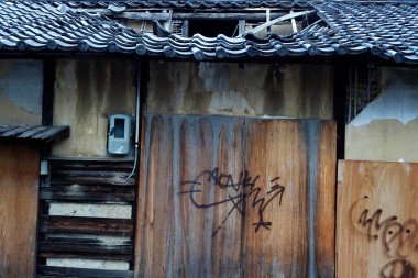 Duvar yazısı ve hasarlı çatı kiremitleri olan terk edilmiş bir bina.